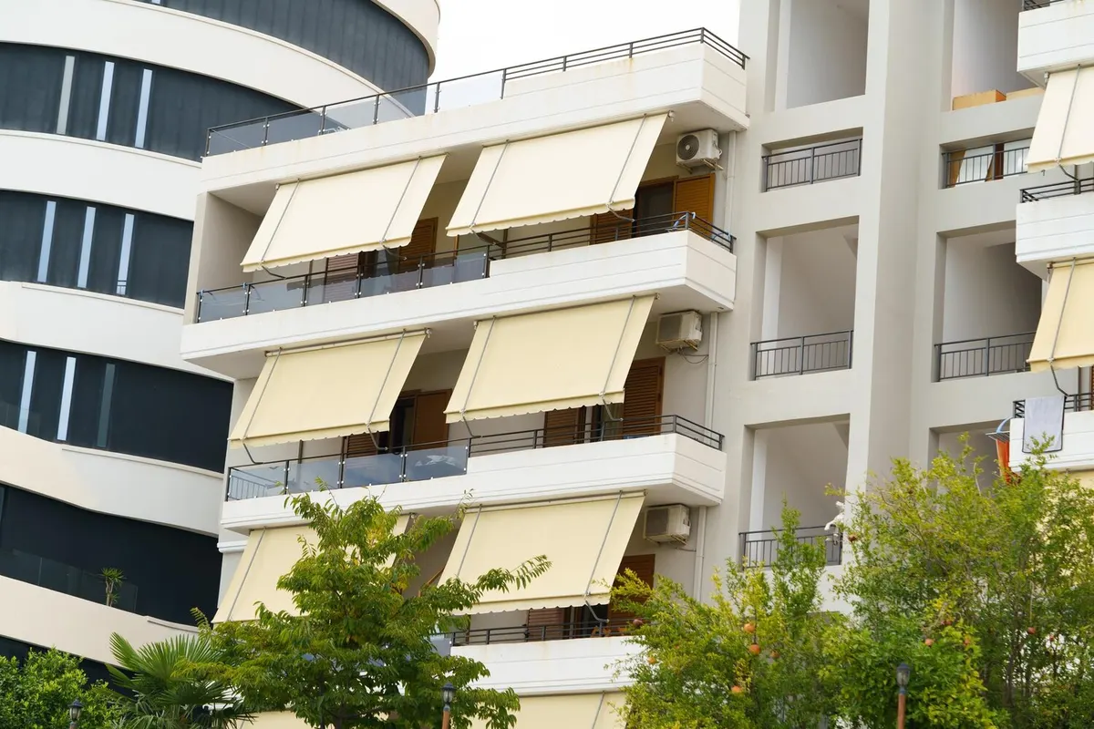 Immeuble blanc aux balcons filants équipés de stores à projection beiges, à côté d'une façade courbe à fenêtres en bandeau